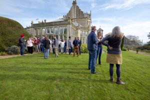 A group of people chatting on a lawn in front of a stately home