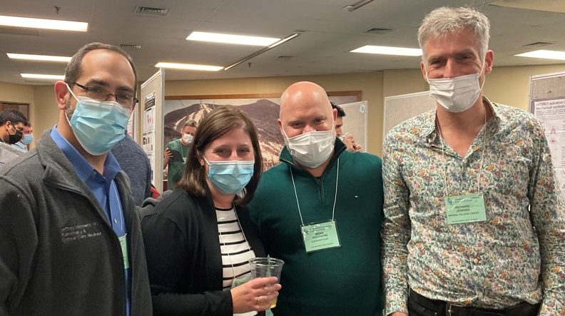 Four people wearing masks posing for the camera in a conference hall