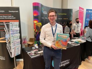 A person holding a board game and standing in front of an exhibition booth