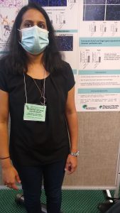 A researcher wearing a mask and standing in front of their research poster
