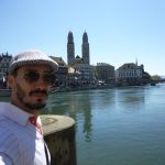 Martin wearing sunglasses in front of a sunny riverside view of Zurich
