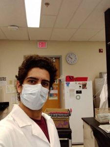 A researcher in the lab wearing a mask and a lab coat