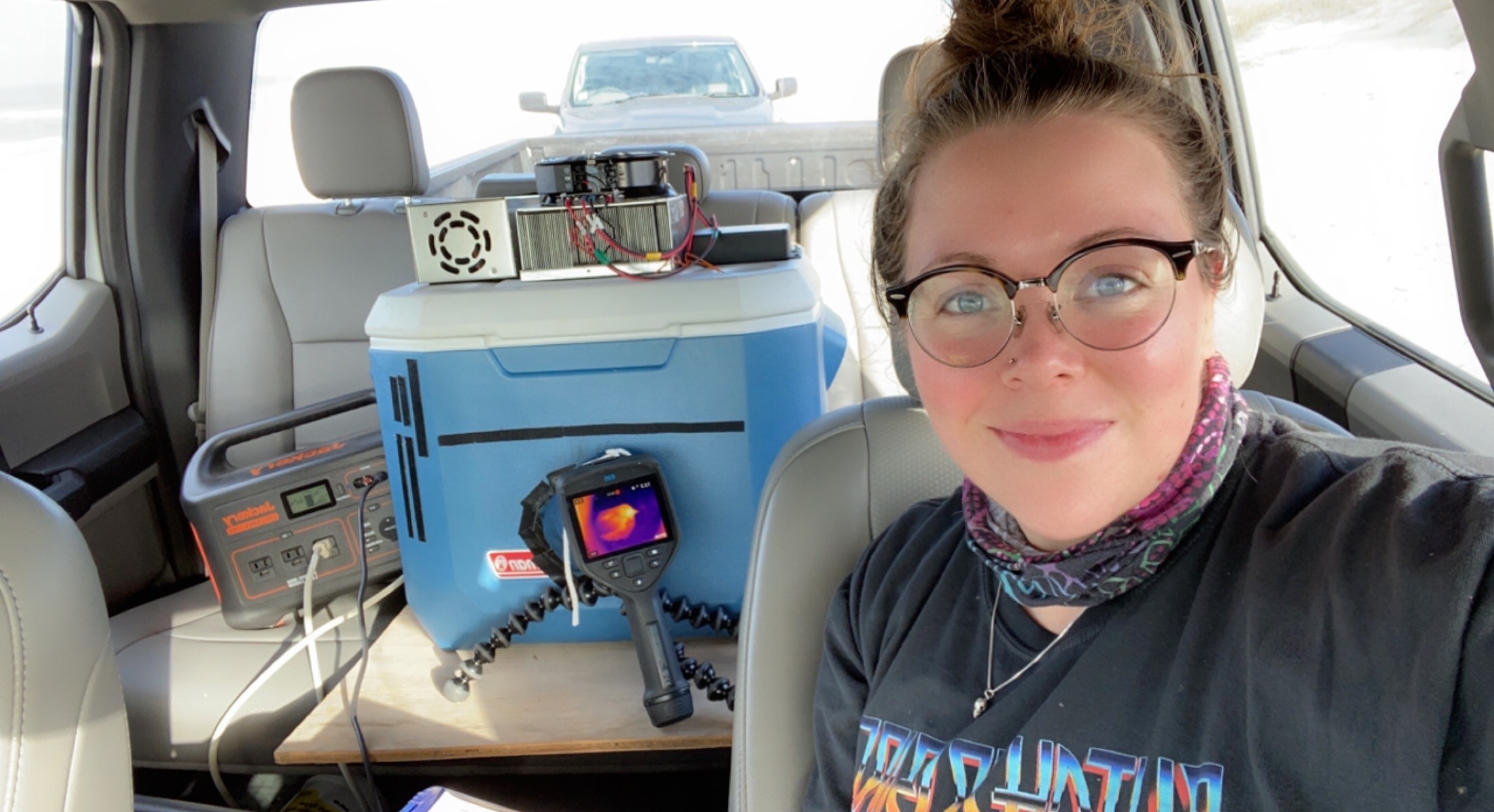 A researcher sitting in a car. Her thermo imaging equipment is on the back seat behind her