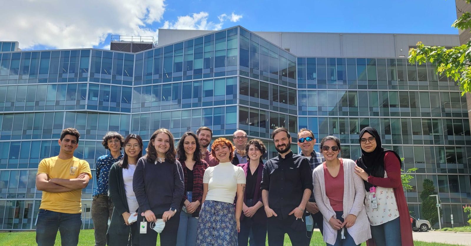 A group of people posing in front of a glass research institute on a sunny day