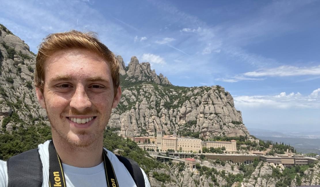 Anthony standing in front of a monastery built into the side of a mountain. 