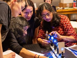 Four summer school attendees working together to assemble a microscope on a rail. 