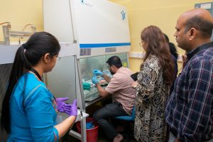 Attendees are gathered round a fume hood, where someone is sitting down and working.