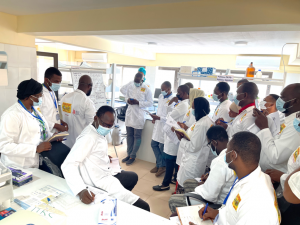A group of researchers in lab coats listening to a demonstrator