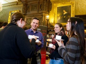 Four people chatting over coffee in a room decorated with paintings